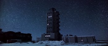Movie still from “Airport” (1970), directed by George Seaton – A tall building in the middle of a snowy field at night; Extreme Wide shot, Low angle