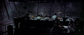 Movie still from “Airport” (1970), directed by George Seaton – A group of men sitting at a table in front of a window; Extreme Wide shot, High angle