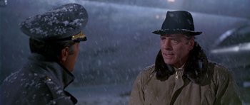 Movie still from “Airport” (1970), directed by George Seaton – A man wearing a hat and a jacket talking to another man in the snow; Close Up shot, Over the shoulder angle