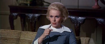Movie still from “Airport” (1970), directed by George Seaton – A woman pointing to her ear while wearing a suit; Close Up shot, Over the shoulder angle