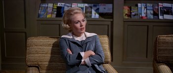 Movie still from “Airport” (1970), directed by George Seaton – A woman sitting in a chair with her arms crossed; Medium shot, Low angle