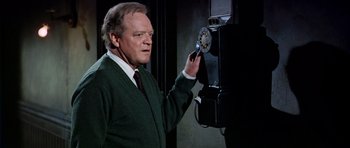 Movie still from “Airport” (1970), directed by George Seaton – An older man in a green sweater holding a phone; Medium shot, High angle