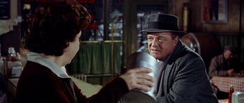 Movie still from “Airport” (1970), directed by George Seaton – An older man in a hat is holding a drink; Medium shot, Over the shoulder angle