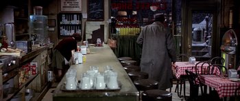 Movie still from “Airport” (1970), directed by George Seaton – A man standing in front of a counter with a bunch of cups on it; Wide shot, High angle