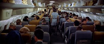 Movie still from “Airport” (1970), directed by George Seaton – A group of people sitting on a plane in the middle of the aisle; Wide shot, High angle