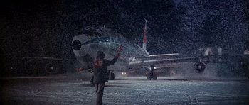Movie still from “Airport” (1970), directed by George Seaton – A man standing in front of an airplane on a snowy night; Extreme Wide shot, High angle