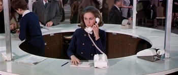 Movie still from “Airport” (1970), directed by George Seaton – A woman sitting at a counter talking on a phone; Medium shot, High angle