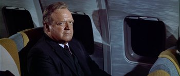 Movie still from “Airport” (1970), directed by George Seaton – A man in a suit and tie sitting on a plane; Close Up shot, Low angle