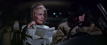 Movie still from “Airport” (1970), directed by George Seaton – A woman sitting in the back seat of a car; Medium shot, Over the shoulder angle