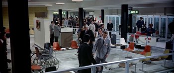 Movie still from “Airport” (1970), directed by George Seaton – A group of people standing around in a room; Extreme Wide shot, High angle