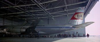 Movie still from “Airport” (1970), directed by George Seaton – People are standing in a hangar next to an airplane; Extreme Wide shot, Low angle