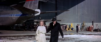 Movie still from “Airport” (1970), directed by George Seaton – An older man and woman are walking in front of an airplane; Wide shot, Low angle