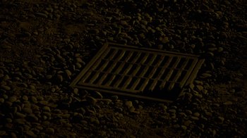 Movie still from “Better Call Saul” (2015), created by Vince Gilligan – A metal grate sitting on top of a gravel ground; Extreme Close Up shot, Overhead angle