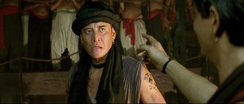 Movie still from “Asoka” (2001), directed by Santosh Sivan – A man with tattoos on his arms and a black hat; Close Up shot, Over the shoulder angle