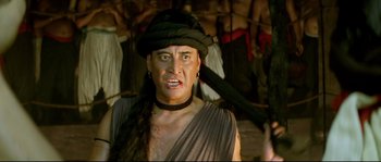 Movie still from “Asoka” (2001), directed by Santosh Sivan – A man in a black hat and a brown shirt; Close Up shot, Low angle