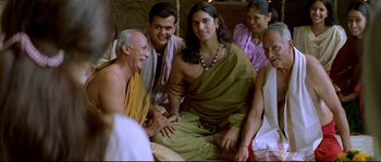 Movie still from “Asoka” (2001), directed by Santosh Sivan – A group of people sitting around a man in a green shirt; Medium shot, High angle