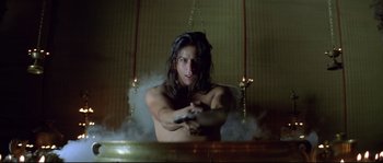 Movie still from “Asoka” (2001), directed by Santosh Sivan – A man with long hair is holding a remote control; Medium shot, Low angle