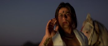 Movie still from “Asoka” (2001), directed by Santosh Sivan – A man with long black hair wearing a white shirt; Close Up shot, Low angle
