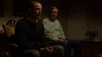 Movie still from “Better Call Saul” (2015), created by Vince Gilligan – Two men sitting on a couch in a dark room; Medium shot, Over the shoulder angle