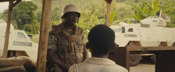 Movie still from “Beasts of No Nation” (2015), directed by Cary Joji Fukunaga – A man in a military uniform talking to another man; Medium shot, Over the shoulder angle