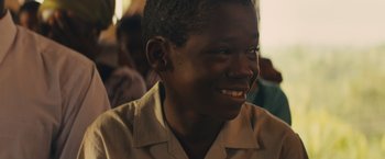 Movie still from “Beasts of No Nation” (2015), directed by Cary Joji Fukunaga – A young person smiling for the camera; Close Up shot, Over the shoulder angle