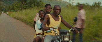 Movie still from “Beasts of No Nation” (2015), directed by Cary Joji Fukunaga – A group of people on a motorcycle on a dirt road; Medium shot, Low angle