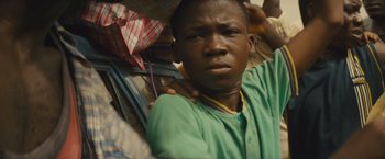Movie still from “Beasts of No Nation” (2015), directed by Cary Joji Fukunaga – A young man is sitting on a pile of luggage; Close Up shot, Low angle