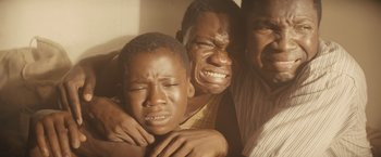Movie still from “Beasts of No Nation” (2015), directed by Cary Joji Fukunaga – Two men and a boy are hugging and one is crying; Close Up shot, Low angle