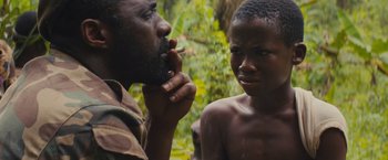 Movie still from “Beasts of No Nation” (2015), directed by Cary Joji Fukunaga – A man smoking a cigarette next to a young boy; Close Up shot, Over the shoulder angle