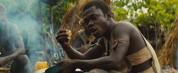 Movie still from “Beasts of No Nation” (2015), directed by Cary Joji Fukunaga – A man eating a piece of food while sitting on a bench; Close Up shot, Low angle