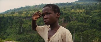 Movie still from “Beasts of No Nation” (2015), directed by Cary Joji Fukunaga – A young man saluting in front of a forest; Close Up shot, Low angle