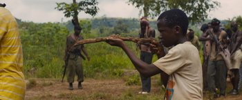 Movie still from “Beasts of No Nation” (2015), directed by Cary Joji Fukunaga – A man holding a stick in a field; Medium shot, Over the shoulder angle