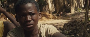 Movie still from “Beasts of No Nation” (2015), directed by Cary Joji Fukunaga – A young man is sitting in the woods; Close Up shot, High angle