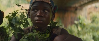 Movie still from “Beasts of No Nation” (2015), directed by Cary Joji Fukunaga – A young boy wearing a hat and holding a bunch of green leaves; Close Up shot, Low angle