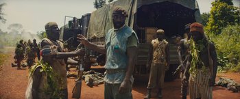 Movie still from “Beasts of No Nation” (2015), directed by Cary Joji Fukunaga – A man holding a rifle in front of an army vehicle; Medium shot, Over the shoulder angle