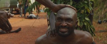 Movie still from “Beasts of No Nation” (2015), directed by Cary Joji Fukunaga – A man is getting his hair combed by another man; Close Up shot, High angle