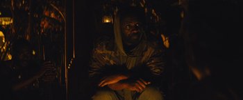 Movie still from “Beasts of No Nation” (2015), directed by Cary Joji Fukunaga – A man sitting in the dark with his arms crossed; Medium shot, High angle