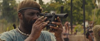 Movie still from “Beasts of No Nation” (2015), directed by Cary Joji Fukunaga – A man with a beard holding a rifle in his hands; Close Up shot, Over the shoulder angle