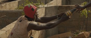 Movie still from “Beasts of No Nation” (2015), directed by Cary Joji Fukunaga – A man in a red helmet is holding his arms up; Medium shot, Low angle
