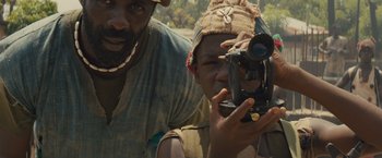 Movie still from “Beasts of No Nation” (2015), directed by Cary Joji Fukunaga – A man standing next to a woman holding a camera; Close Up shot, Low angle