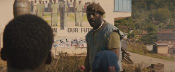 Movie still from “Beasts of No Nation” (2015), directed by Cary Joji Fukunaga – A man in a military uniform walking in front of a mural; Medium shot, Over the shoulder angle