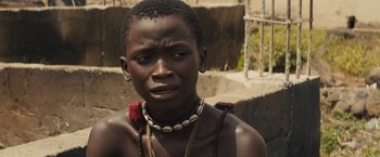 Movie still from “Beasts of No Nation” (2015), directed by Cary Joji Fukunaga – A young man wearing a necklace with shells around his neck; Close Up shot, High angle