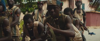 Movie still from “Beasts of No Nation” (2015), directed by Cary Joji Fukunaga – A group of young men standing next to each other holding guns; Medium shot, Low angle