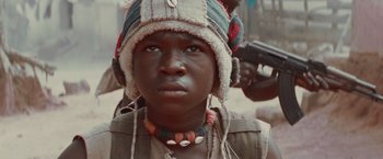 Movie still from “Beasts of No Nation” (2015), directed by Cary Joji Fukunaga – A young boy wearing a hat and a necklace; Close Up shot, Low angle