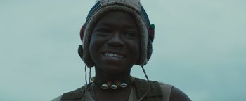 Movie still from “Beasts of No Nation” (2015), directed by Cary Joji Fukunaga – A person wearing a hat and smiling for the camera; Close Up shot, Low angle