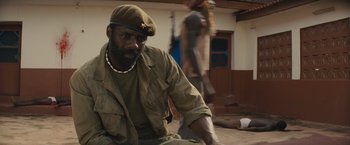 Movie still from “Beasts of No Nation” (2015), directed by Cary Joji Fukunaga – A man in a military uniform sitting on the ground; Close Up shot, High angle