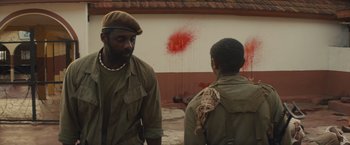 Movie still from “Beasts of No Nation” (2015), directed by Cary Joji Fukunaga – Two men standing next to each other in front of a wall; Medium shot, Over the shoulder angle