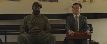 Movie still from “Beasts of No Nation” (2015), directed by Cary Joji Fukunaga – Two men in suits sitting on a bench; Medium shot, Over the shoulder angle