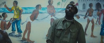 Movie still from “Beasts of No Nation” (2015), directed by Cary Joji Fukunaga – A man standing in front of a painting; Medium shot, Low angle