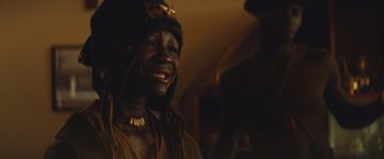 Movie still from “Beasts of No Nation” (2015), directed by Cary Joji Fukunaga – A man with a hat and a necklace smiles for the camera; Close Up shot, Low angle